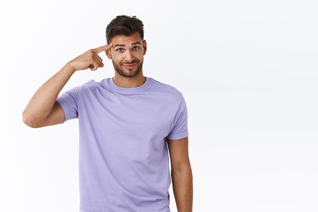 Quelqu'un est fou Un jeune barbu mécontent fait rouler l'index sur la tempe et regarde avec incrédulité ou dédain un sourire narquois maladroit réagir sur une personne agissant de manière stupide ou folle sur fond blanc