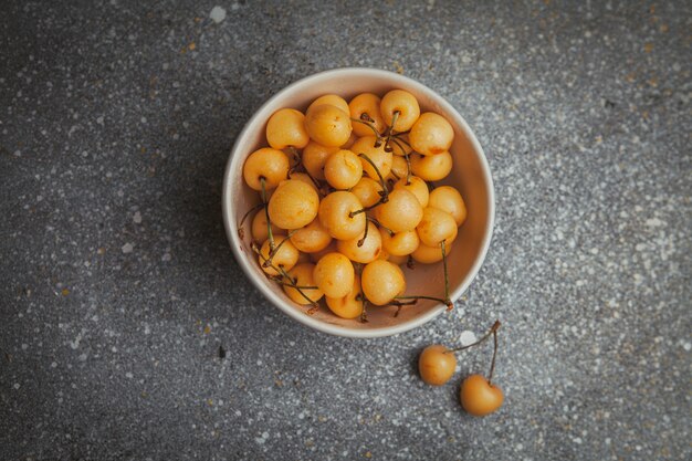 Quelques cerises plus pluvieuses dans un bol sur fond gris texturé,