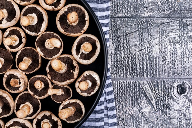 Quelques champignons retournés dans une casserole, sur un tissu apicnic, table en bois gris