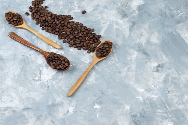 Quelques Grains De Café Dans Des Cuillères En Bois Sur Fond De Plâtre Gris, à Plat.