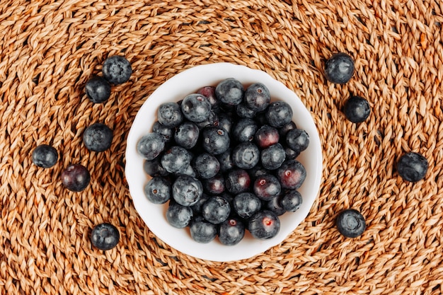 Quelques olives noires dans un bol sur fond de dessous de plat en rotin, vue de dessus.