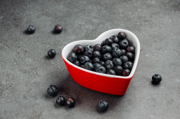 Quelques olives noires dans un bol en forme de coeur rouge sur fond gris, high angle view.