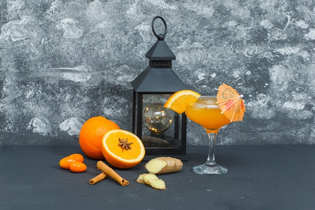 Quelques oranges avec de la lumière antique, du jus dans un verre, du gingembre et des tranches sur une surface texturée, vue latérale.
