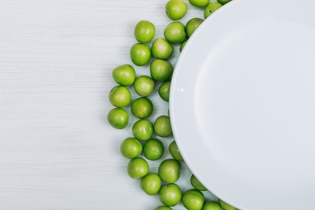 Quelques prunes cerises vertes avec assiette vide sur fond de bois blanc, gros plan. copier l'espace pour le texte