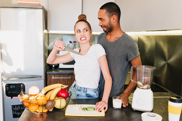 Querelle de famille dans la cuisine. Fille au visage en colère avec un couteau et un mec surpris. Le mari et la femme se disputent, incompréhension, relations brisées, visage irrité, querelle d'imitation.