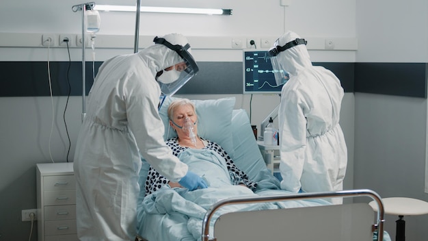 Équipe d'ambulanciers paramédicaux en combinaisons de matières dangereuses vérifiant les soins de santé des patients. Personnel médical protégé contre l'épidémie de coronavirus consultant une femme avec tube à oxygène dans la zone d'isolement de quarantaine