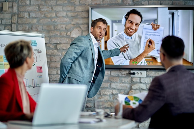 Équipe commerciale ayant une vidéoconférence avec leur collègue lors de la réunion au bureau