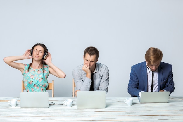 Équipe commerciale travaillant ensemble au bureau sur fond gris clair. tous travaillant sur des ordinateurs portables. fille dans les écouteurs appréciant la musique