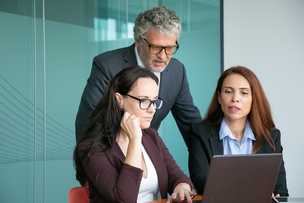 Équipe commerciale de trois regarder la présentation sur ordinateur, regardant l'affichage, discuter des détails