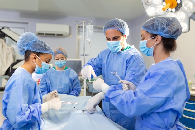 Équipe diversifiée d'assistants de chirurgiens professionnels et d'infirmières effectuant une chirurgie invasive sur un patient à l'hôpital Les chirurgiens de la salle d'opération parlent et utilisent des instruments Un véritable hôpital moderne