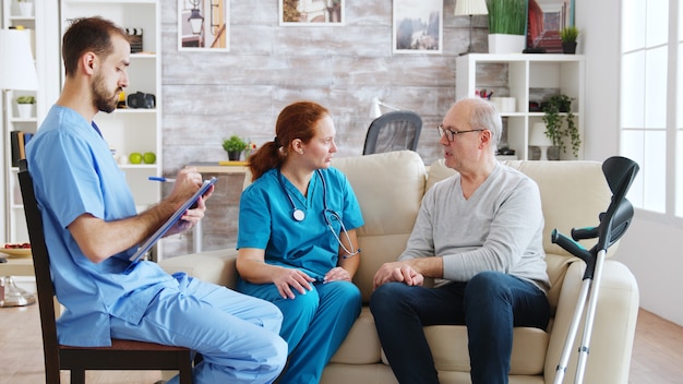 Équipe d'infirmières et d'infirmiers discutant avec un vieil homme à la retraite dans une maison de retraite lumineuse et confortable