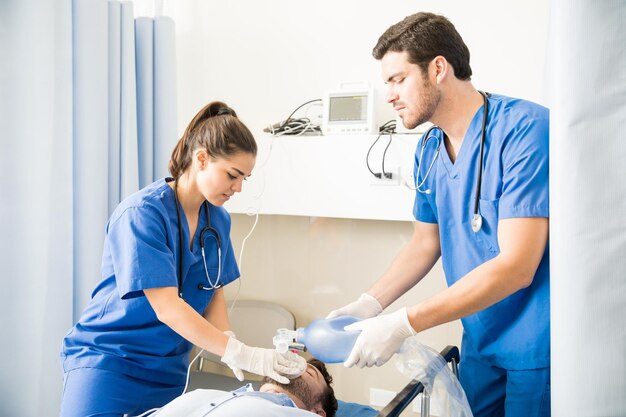 Équipe de médecins masculins et féminins utilisant un sac ambu pour la ventilation d'un patient inconscient