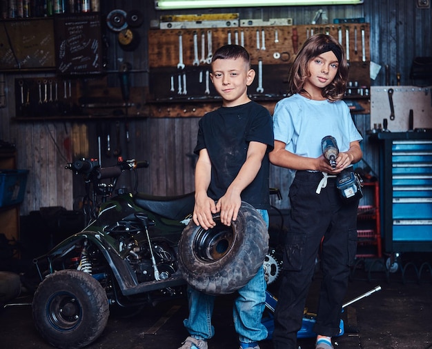 Équipe de rêve en action - deux enfants s'amusent en posant pour un photographe dans un atelier automobile.