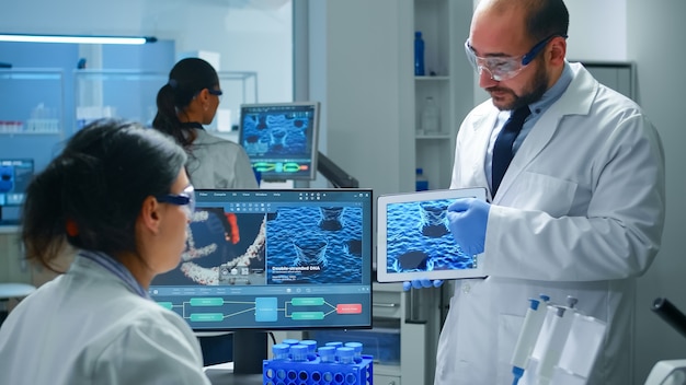 Équipe de scientifiques industriels, d'ingénieurs, de développeurs innovants pour un nouveau vaccin, médecin pointant sur une tablette expliquant l'évolution du virus à un collègue