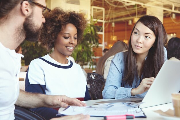 Équipe se réunissant dans un espace de coworking, discutant des plans et de la vision, créant de nouvelles solutions et stratégies commerciales à l'aide d'un ordinateur portable.