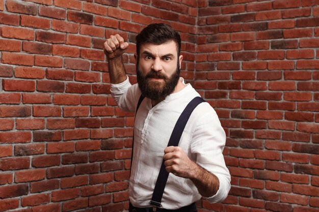 Rage de colère jeune homme montrant les poings posant sur le mur de briques.