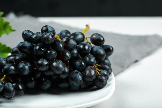 Raisin noir avec feuille sur plaque blanche avec nappe grise. Photo de haute qualité