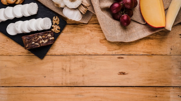 Les raisins; ail et variété de fromages sur textile en jute sur planche de bois