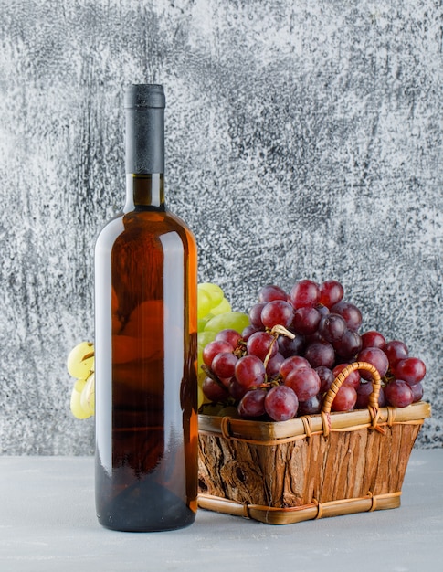 Raisins avec bouteille de boisson dans un panier sur plâtre et grungy, vue latérale.