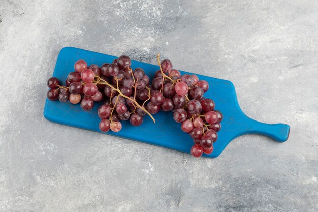 Raisins frais rouges placés sur une planche à découper bleue.