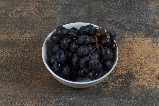 Raisins noirs frais dans un bol blanc.