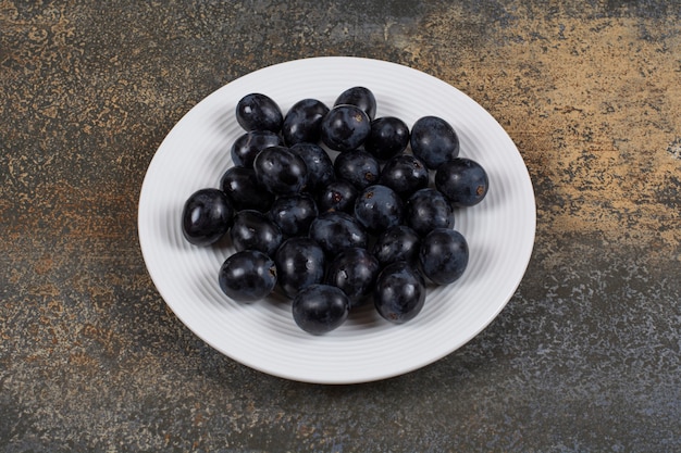 Raisins noirs frais sur plaque blanche.