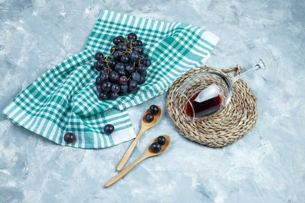 Raisins noirs à plat dans des cuillères en bois avec un verre de vin, napperon sur fond de plâtre et torchon de cuisine. horizontal
