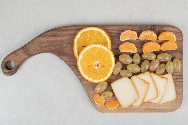 Raisins, oranges, mandarines et fromage sur planche de bois