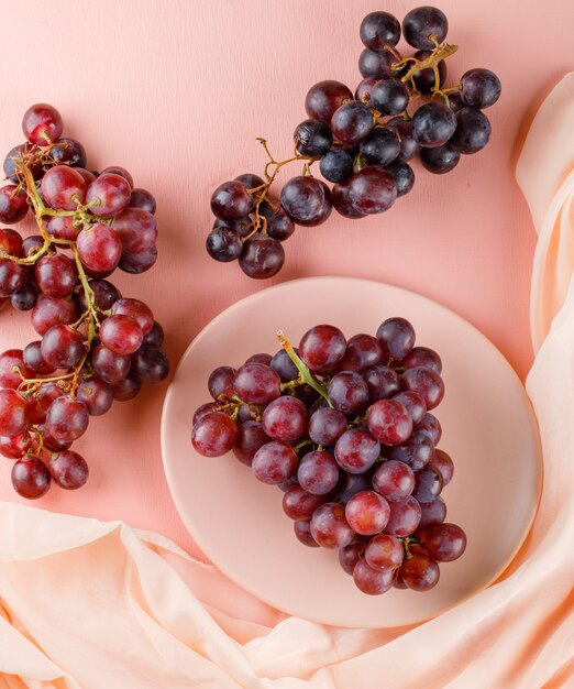 Raisins rouges dans une assiette sur rose et textile.