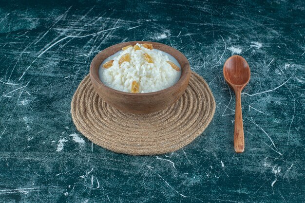 Raisins secs sur un bol de riz au lait à côté d'une cuillère , sur fond bleu. photo de haute qualité