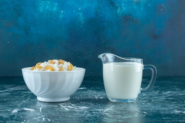 Raisins secs sur un bol de riz au lait à côté d'un verre de lait, sur fond bleu. photo de haute qualité