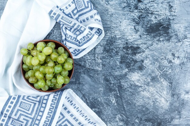 Raisins verts dans un bol d'argile sur fond de plâtre grungy et torchon de cuisine. pose à plat.