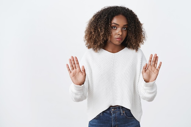 Ralentis, je t'interdis. Une femme sérieuse, mécontente et stricte, autoritaire et séduisante, levant les paumes des mains pour avertir et arrêter de froncer les sourcils en étant mécontente et réticente, en désaccord sur le mur blanc.