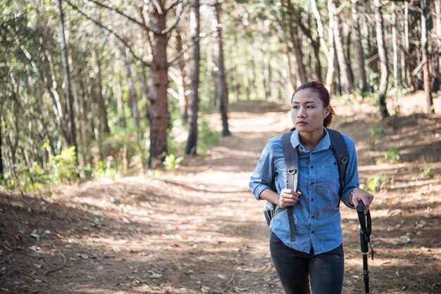 Randonneur aux femmes avec un sac à dos qui traverse une forêt de pins.