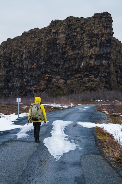 Photo gratuite randonneur dans une veste jaune marchant à travers la route entourée de rochers et d'un champ en islande