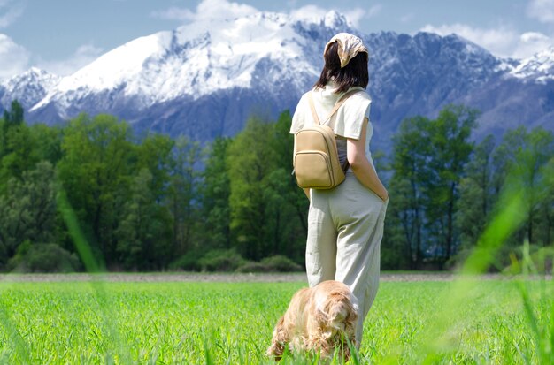 Randonneuse marchant dans le champ vert avec son chien et regardant les montagnes enneigées