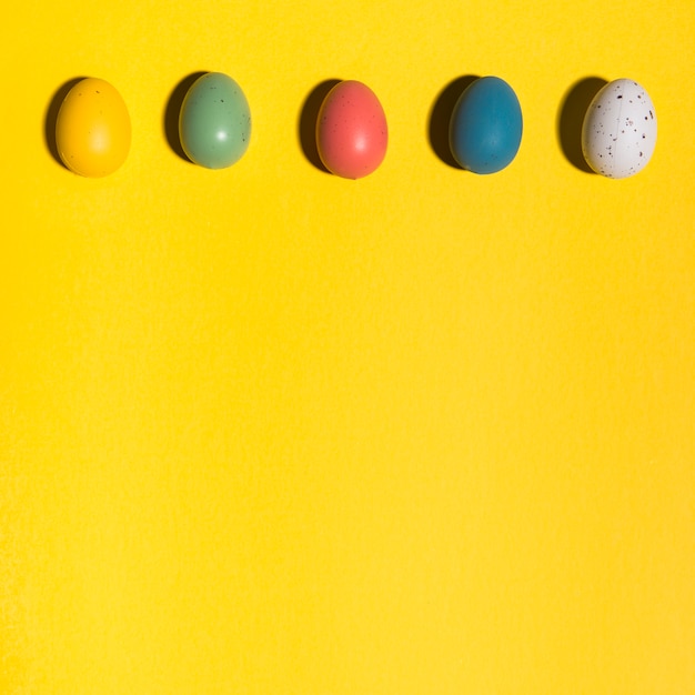 Rangée d&#39;oeufs de Pâques colorés sur une table jaune