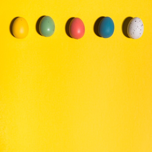 Rangée d&#39;oeufs de Pâques colorés sur une table jaune