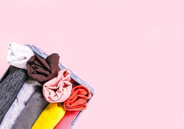 Rangement vertical des vêtements colorés dans la garde-robe de la maison. articles d'habillement dans une boîte textile sur fond rose tendre.