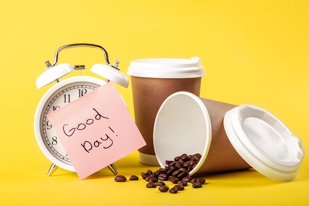 Rappel de papier de tasse de papier de réveil et grains de café sur le fond jaune