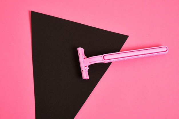 Un rasoir jetable en plastique rose et un triangle noir en papier sur fond rose, une association sur le thème du féminisme et du rasage des poils d'un corps féminin