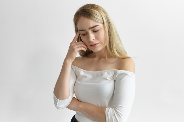 Réaction humaine, émotions et sentiments. Photo de jolie jeune femme de race blanche portant haut élégant étant frustré par des problèmes financiers, tenant le doigt sur sa tempe, ayant un regard réfléchi