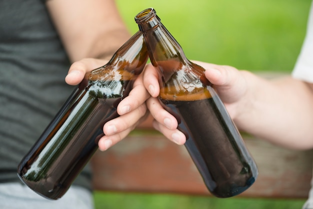 Photo gratuite recadrer les gars clink bouteilles sur banc dans le parc