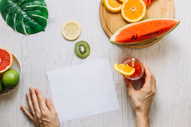 Recadrer les mains avec du smoothie près des fruits et de la feuille de papier