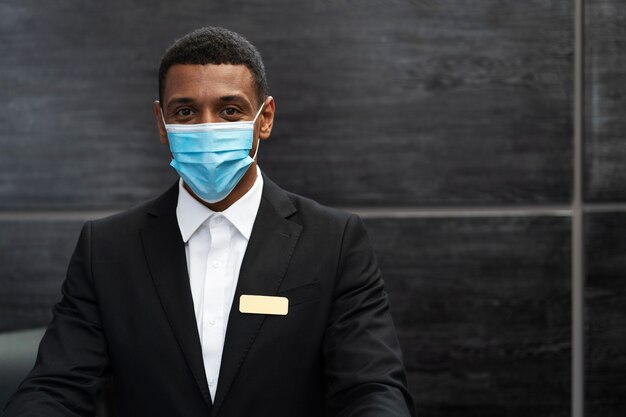 Réceptionniste masculin en costume au travail portant un masque médical
