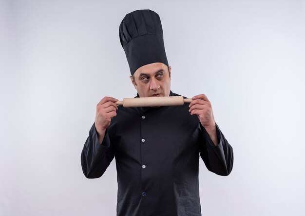 À la recherche à côté homme d'âge moyen cuisinier en uniforme de chef holding rouleau à pâtisserie sur mur blanc isolé