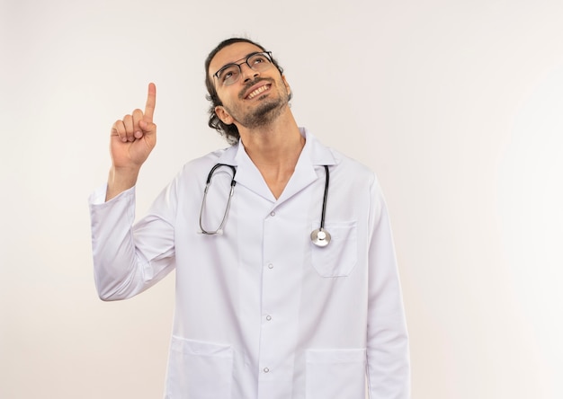 À la recherche d'un jeune médecin de sexe masculin souriant avec des lunettes optiques portant une robe blanche avec un stéthoscope vers le haut