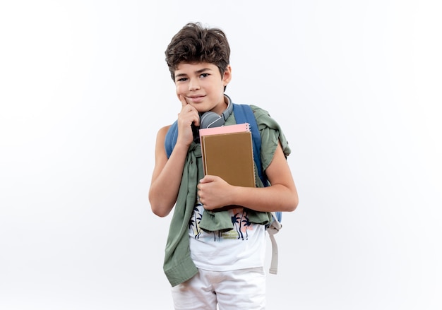 À la recherche d'un petit écolier portant un sac à dos et un casque tenant un livre et mettant le doigt sur la joue