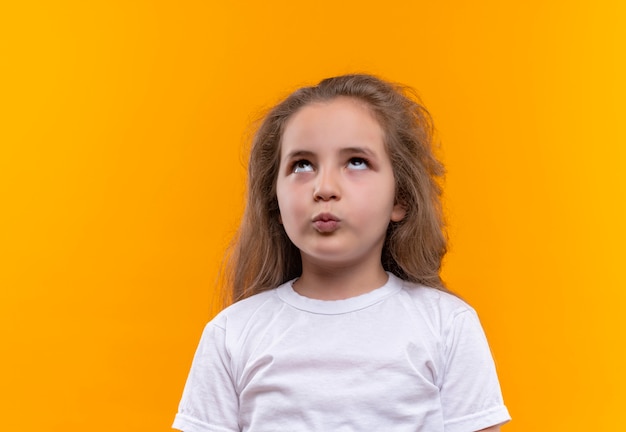 À la recherche de petite écolière portant un t-shirt blanc montrant le geste de baiser sur fond orange isolé