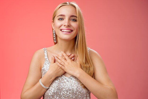 Reconnaissante charmante femme blonde européenne des années 25 en robe de soirée argentée appuyez sur le cœur des paumes se sentent reconnaissants apprécient les efforts chérissent le geste romantique reçoivent des compliments flatteurs, souriant joyeusement.